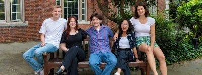 2024/25 Officer Trustees sitting on a bench outside in Beit Quad. They are smiling and seated together.