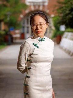 A portrait photograph of Yi Yang, a Chinese female in her 20s, in Beit Quad. Yi is wearing a white dress with green decorative bows, and is wearing glasses.